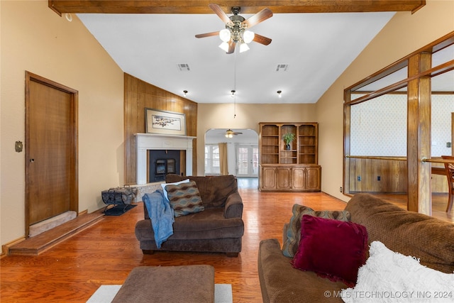 living room featuring a large fireplace, ceiling fan, wooden walls, hardwood / wood-style flooring, and vaulted ceiling with beams