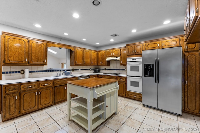 kitchen with stainless steel fridge, white double oven, gas stovetop, sink, and light tile patterned floors