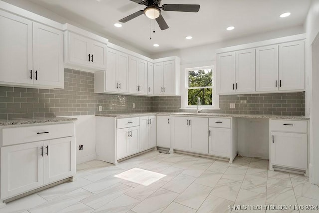 kitchen featuring backsplash, light stone counters, ceiling fan, sink, and white cabinetry