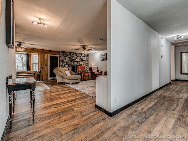 living room with wood-type flooring, a textured ceiling, a stone fireplace, and ceiling fan