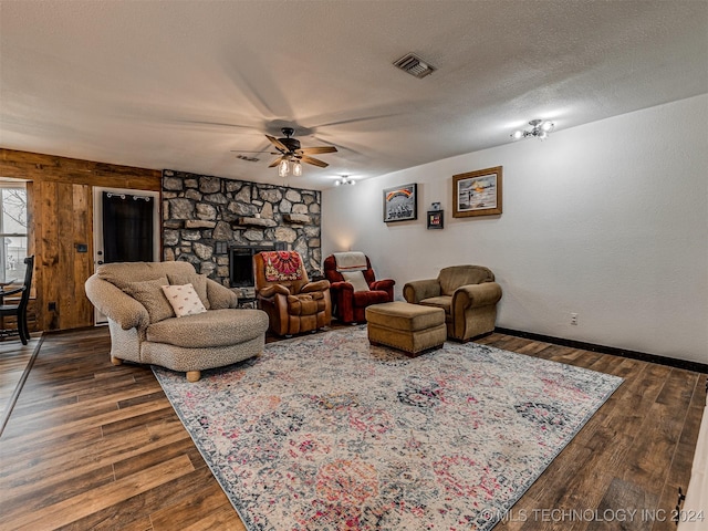 living room with a stone fireplace, ceiling fan, dark wood-type flooring, and a textured ceiling