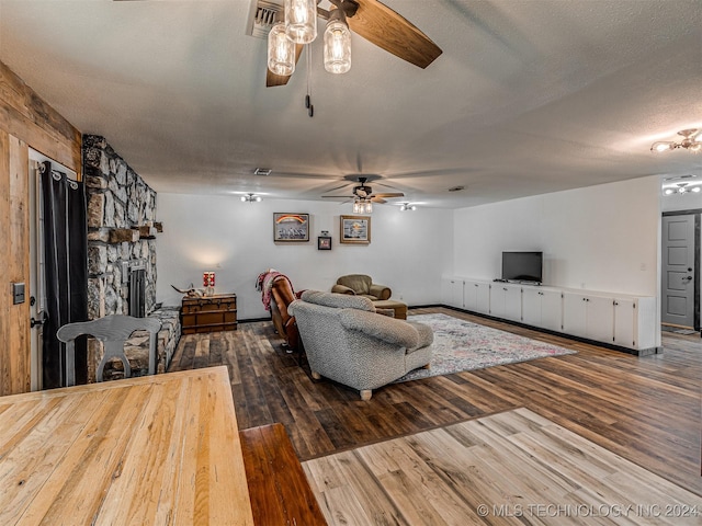 living room featuring hardwood / wood-style floors, ceiling fan, a stone fireplace, and a textured ceiling