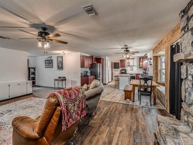 living room with ceiling fan, a textured ceiling, and light wood-type flooring