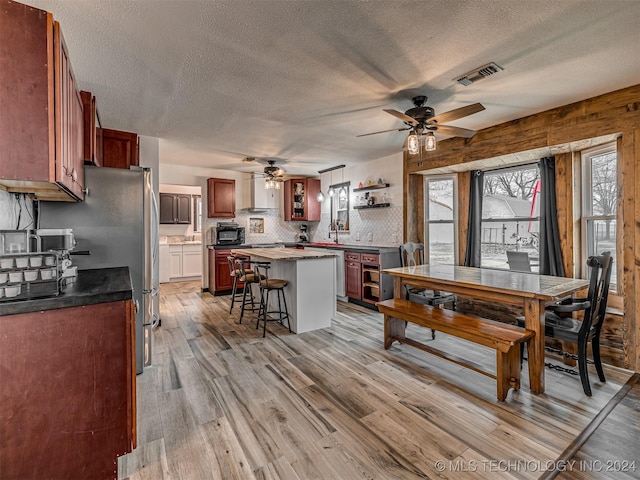 dining room with ceiling fan, wood walls, a textured ceiling, and light wood-type flooring