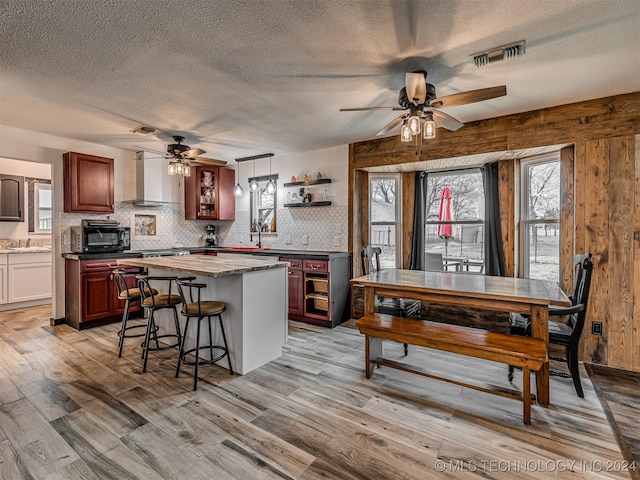 kitchen featuring decorative light fixtures, light hardwood / wood-style flooring, ceiling fan, and wall chimney range hood