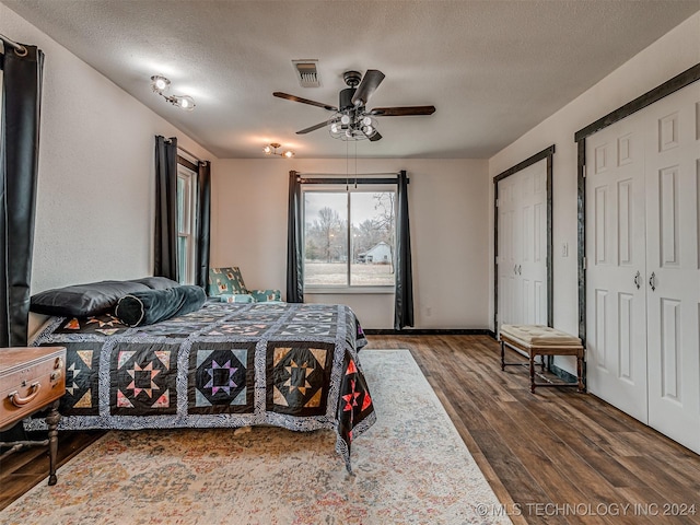 bedroom with ceiling fan, dark hardwood / wood-style flooring, a textured ceiling, and two closets