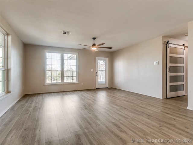 empty room with a barn door, ceiling fan, and light hardwood / wood-style flooring