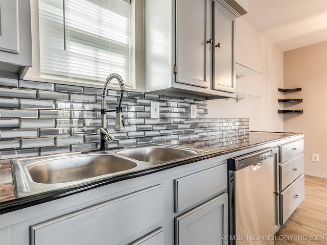 kitchen with gray cabinetry, sink, light hardwood / wood-style flooring, stainless steel dishwasher, and tasteful backsplash