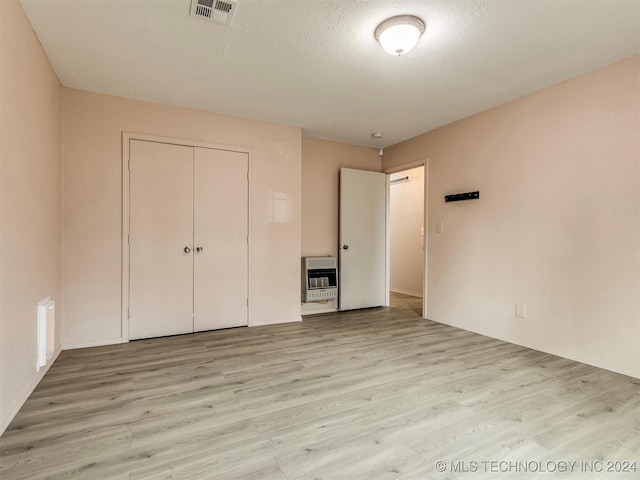 unfurnished bedroom with heating unit, light wood-type flooring, a textured ceiling, and a closet