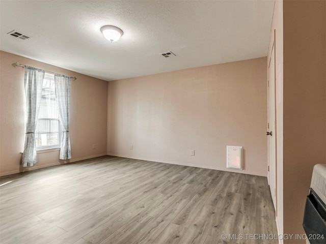 spare room with heating unit, light hardwood / wood-style flooring, and a healthy amount of sunlight