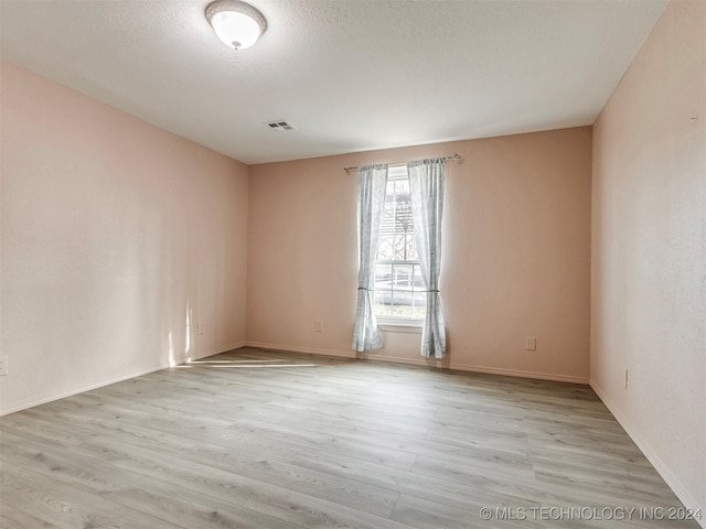 unfurnished room with a textured ceiling and light wood-type flooring