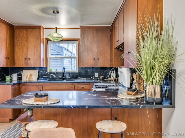 kitchen with dark countertops, brown cabinets, a kitchen breakfast bar, pendant lighting, and a sink