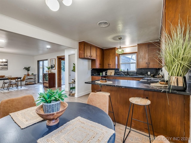 kitchen with visible vents, brown cabinetry, backsplash, a peninsula, and a sink