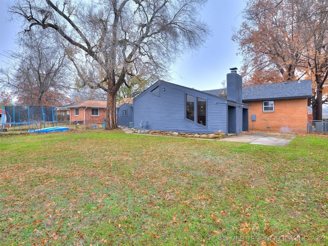 rear view of house with a trampoline, brick siding, a chimney, crawl space, and a patio area