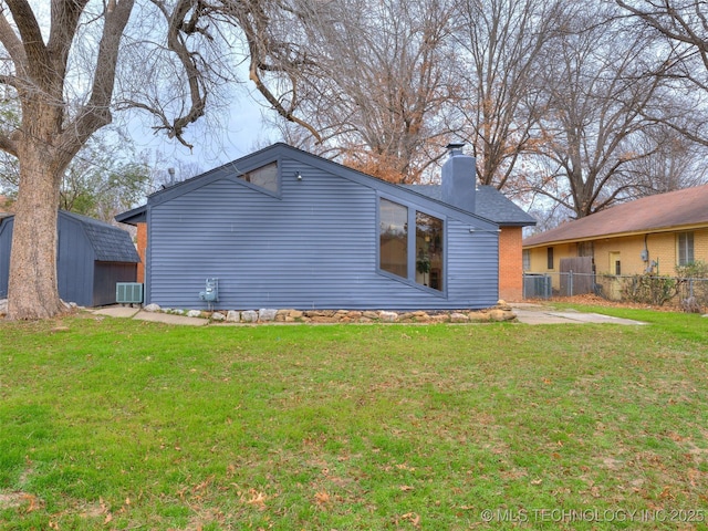 rear view of house featuring cooling unit, a chimney, fence, and a lawn