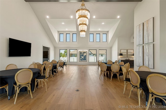 dining area featuring light wood-type flooring, a towering ceiling, and a notable chandelier