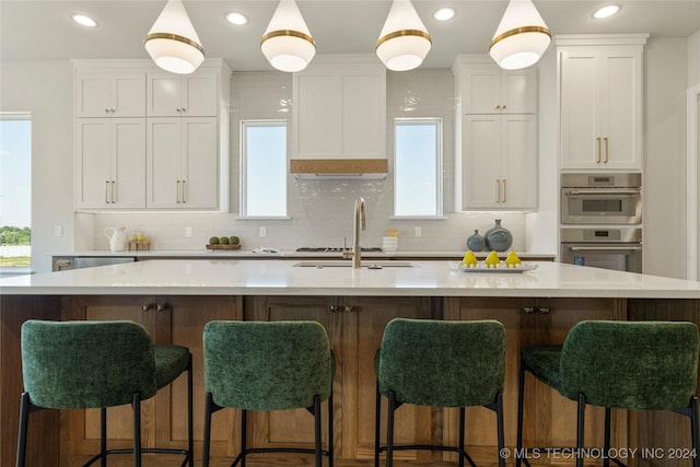 kitchen with white cabinets, decorative backsplash, a spacious island, and sink