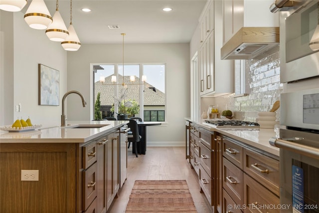 kitchen with a center island with sink, light wood-type flooring, decorative light fixtures, custom range hood, and a chandelier