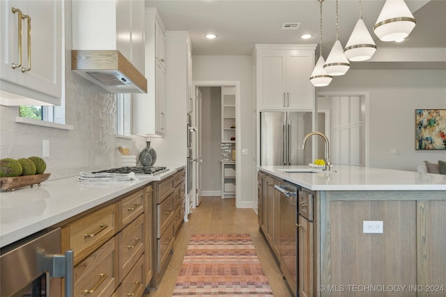 kitchen with wall chimney exhaust hood, hanging light fixtures, beverage cooler, a kitchen island with sink, and white cabinets