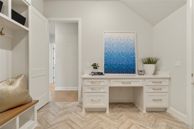 office area with built in desk, vaulted ceiling, and light parquet flooring