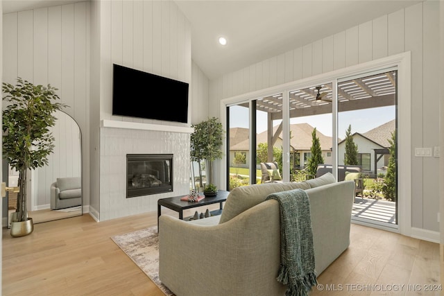 living room featuring a tile fireplace, light wood-type flooring, and lofted ceiling