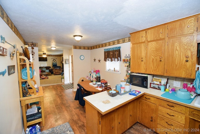 kitchen with kitchen peninsula, dark hardwood / wood-style flooring, a textured ceiling, and backsplash