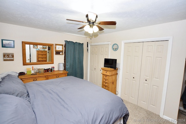 carpeted bedroom with ceiling fan, a textured ceiling, and multiple closets