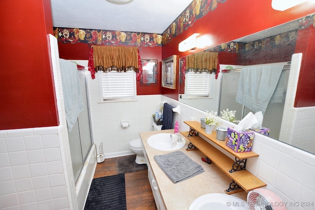 bathroom featuring hardwood / wood-style floors, toilet, vanity, a shower with shower door, and tile walls