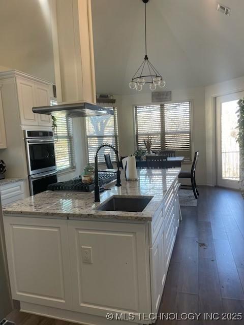 kitchen with stainless steel double oven, white cabinets, hanging light fixtures, light stone counters, and sink