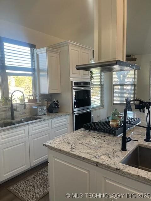 kitchen with light stone countertops, white cabinets, appliances with stainless steel finishes, sink, and island range hood