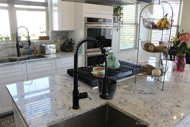 kitchen with light stone countertops, white cabinetry, double oven, and sink