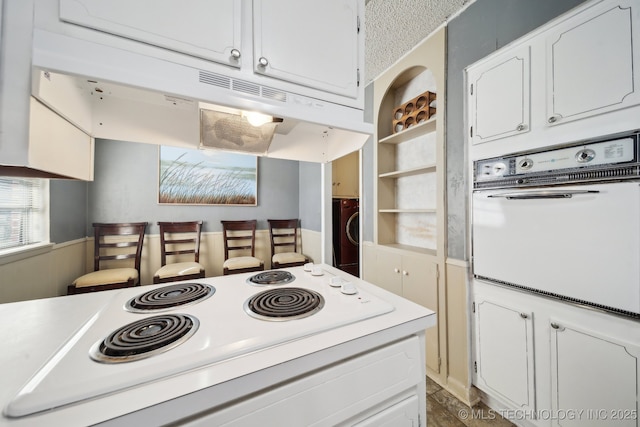 kitchen featuring stacked washer / dryer, white cabinetry, white appliances, and built in shelves