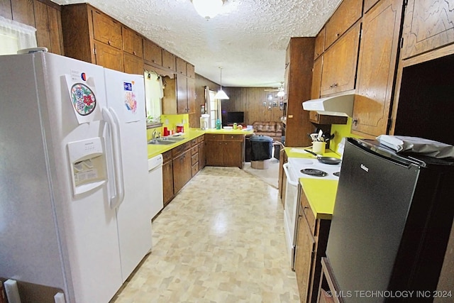 kitchen featuring white appliances, wooden walls, ceiling fan, a textured ceiling, and decorative light fixtures