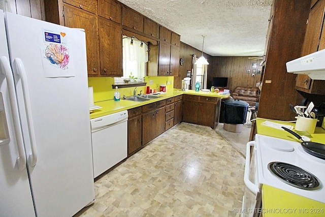 kitchen featuring pendant lighting, white appliances, sink, wooden walls, and a textured ceiling