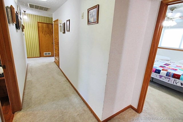 hall with a textured ceiling and light colored carpet