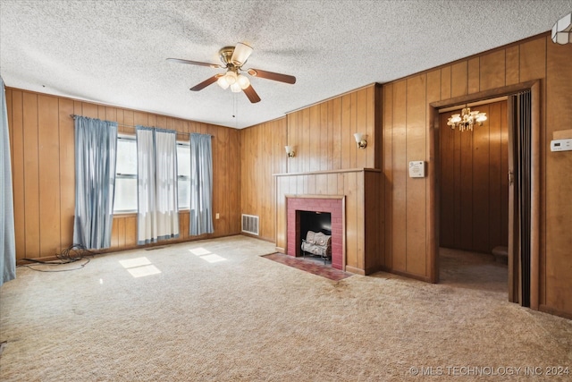 unfurnished living room with ceiling fan with notable chandelier, light colored carpet, wooden walls, and a brick fireplace