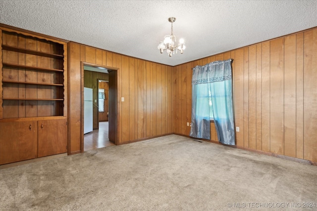 carpeted spare room with built in shelves, wooden walls, a textured ceiling, and a notable chandelier