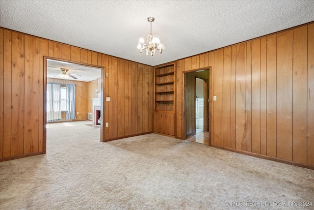 carpeted empty room featuring a textured ceiling, wooden walls, and ceiling fan with notable chandelier