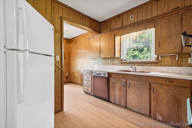 kitchen featuring light wood-type flooring, sink, white refrigerator, dishwasher, and wood walls