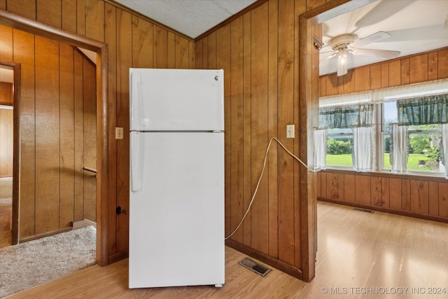 kitchen featuring a textured ceiling, ceiling fan, white refrigerator, light hardwood / wood-style flooring, and wood walls