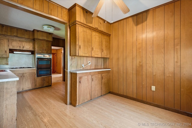 kitchen with gas stovetop, ceiling fan, wooden walls, light hardwood / wood-style flooring, and range hood