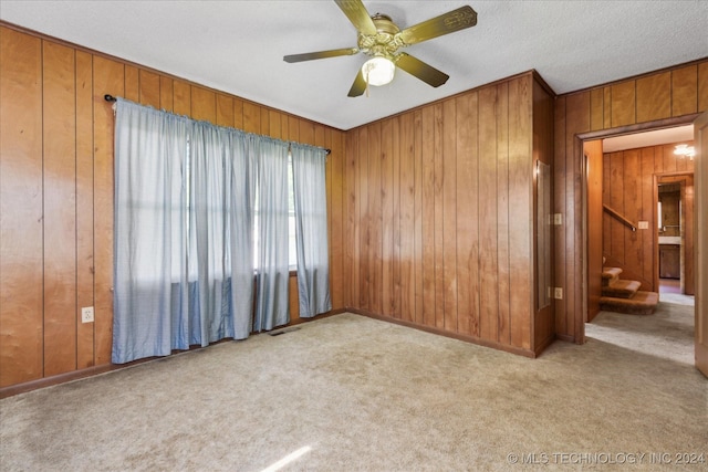 carpeted empty room featuring ceiling fan and wood walls