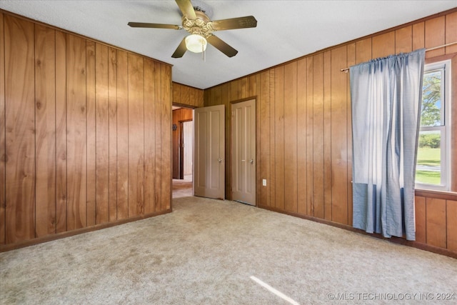 unfurnished bedroom featuring ceiling fan, light carpet, and wood walls