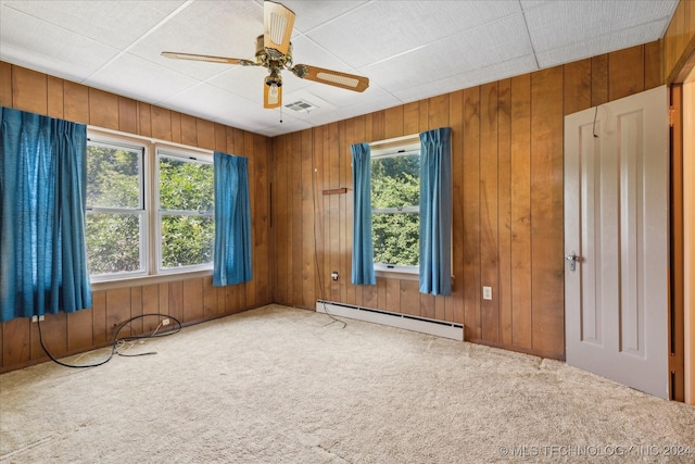 unfurnished room featuring baseboard heating, ceiling fan, carpet flooring, and wood walls