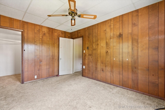 unfurnished bedroom featuring light carpet, a paneled ceiling, ceiling fan, and wooden walls