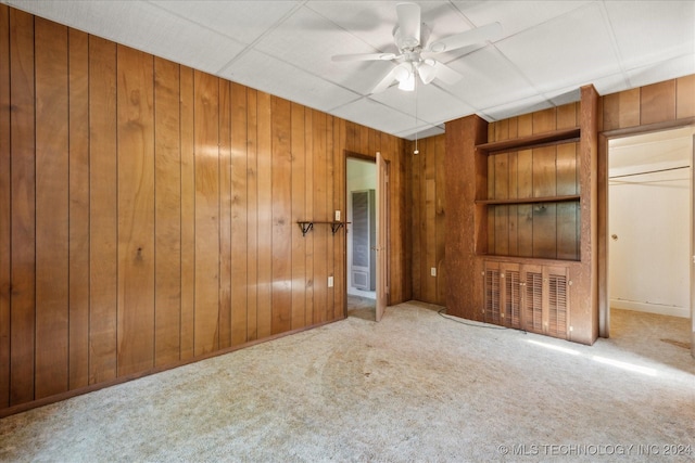 unfurnished bedroom featuring ceiling fan, a drop ceiling, carpet floors, and wooden walls