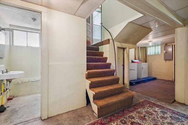 staircase featuring concrete floors, a healthy amount of sunlight, electric panel, and washing machine and clothes dryer