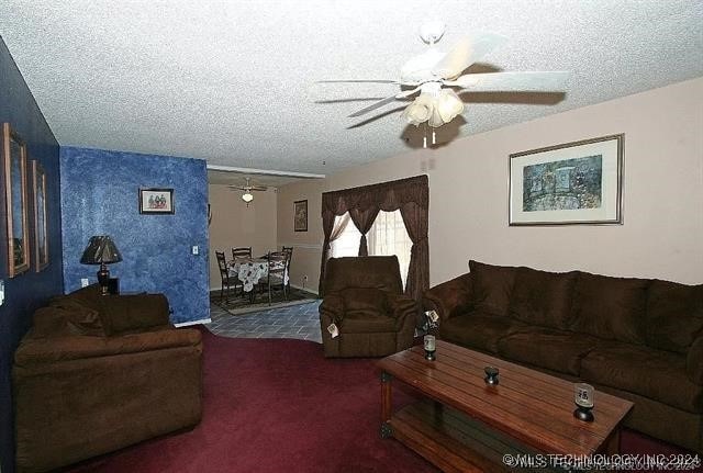 living room featuring a textured ceiling, dark carpet, and ceiling fan