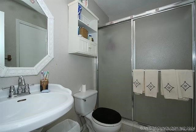 bathroom featuring toilet, a shower with door, and sink