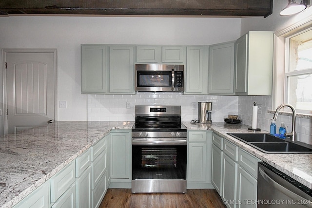 kitchen featuring sink, decorative backsplash, light stone countertops, dark hardwood / wood-style flooring, and stainless steel appliances